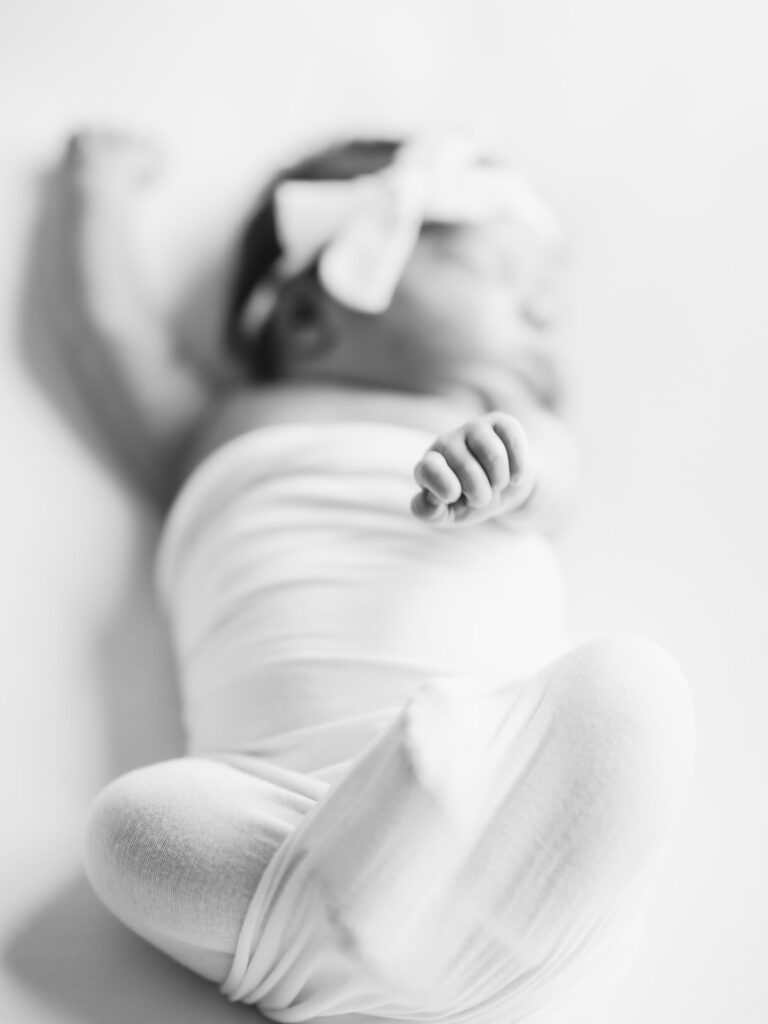 Newborn black and white photo of baby wrapped in white swaddle stretching arms