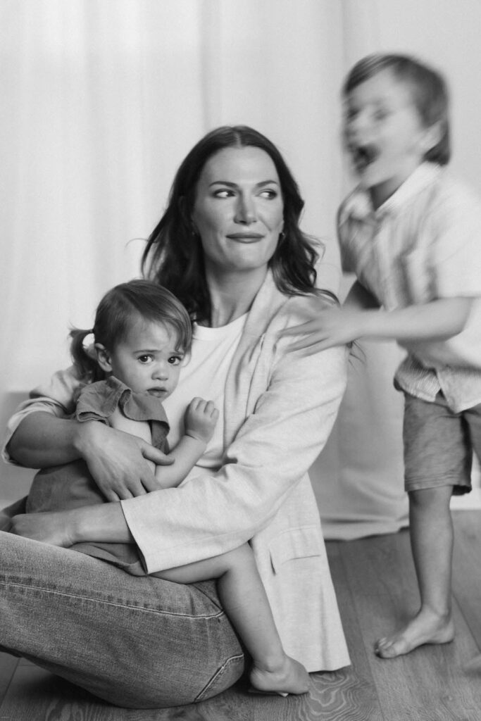 mother holding her toddler girl with her young son moving quickly through the image in black white photography. professional portrait transforming self image