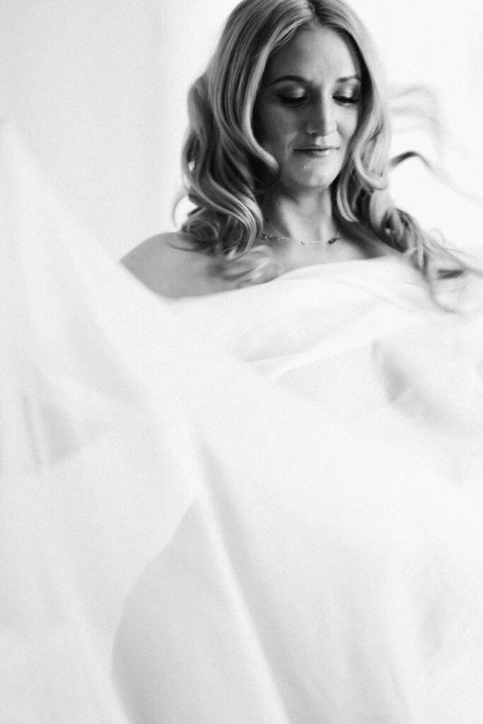 woman dancing during maternity session in black in white photo with sheer sheet covering her body