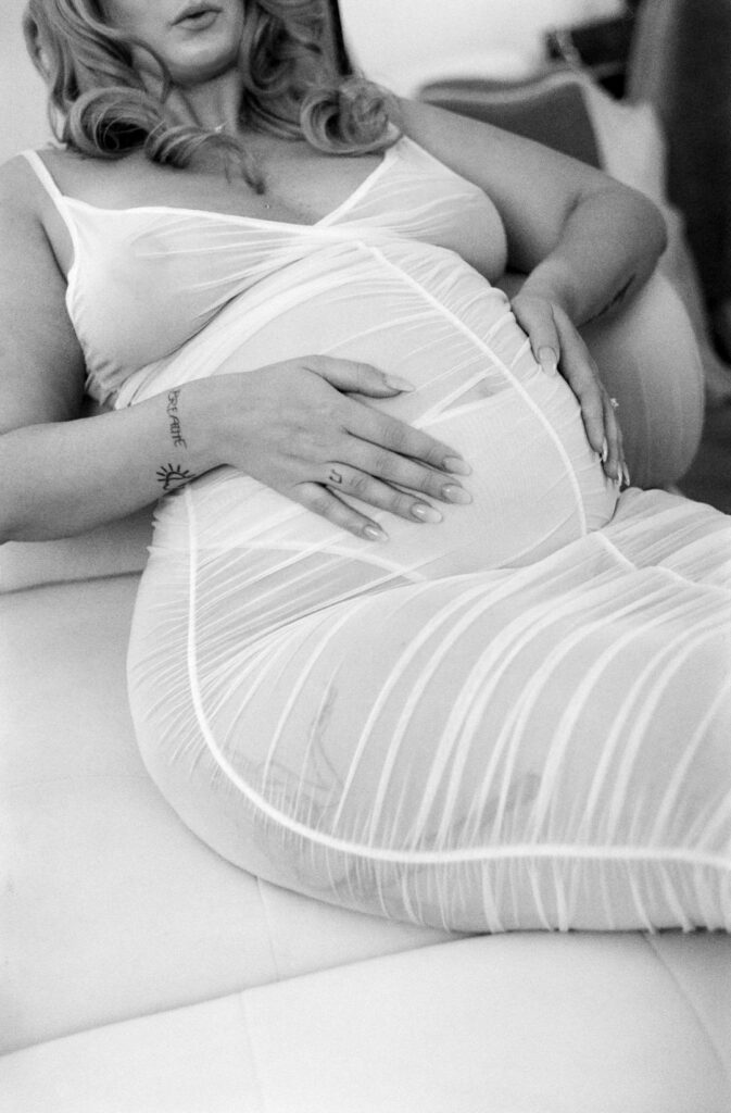 woman laying on chase lounge sofa holding her pregnant belly in black and white photograph