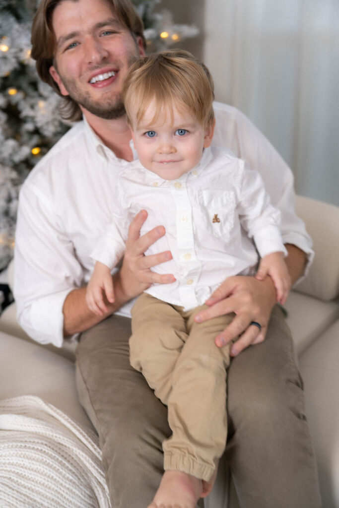 dad holding toddler son in neutral outfit during holiday photo session