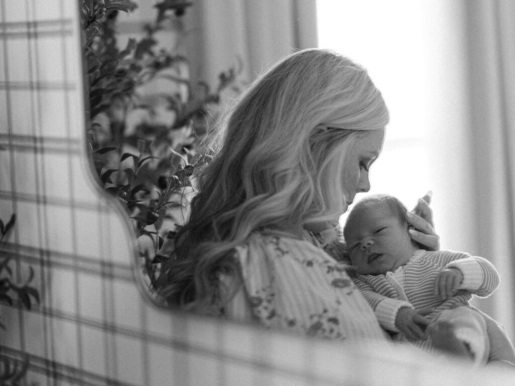 mom holding newborn baby through a decorative mirror in nursery