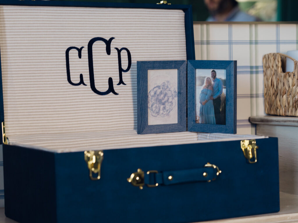 Close up of an embroidered keepsake diy trunk and a framed image of an embryo and a pregnant woman with her husband