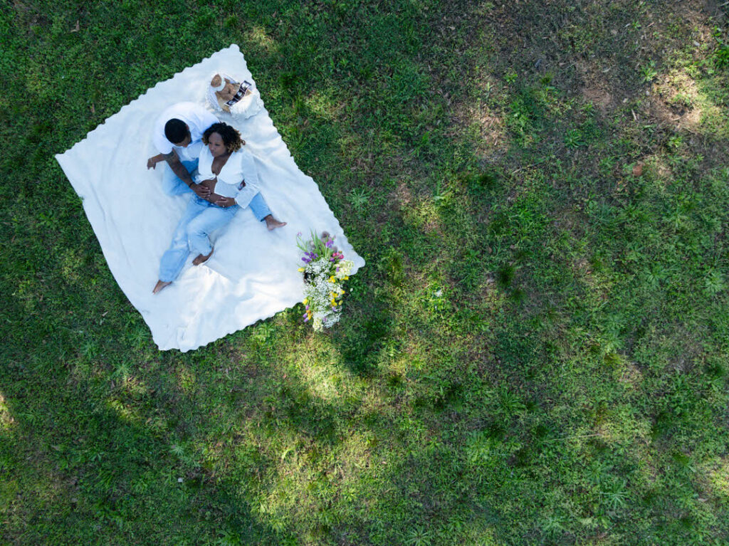 birds eye view from drone camera of a new mom holding her pregnant belly laying on a blanket in beautiful green field