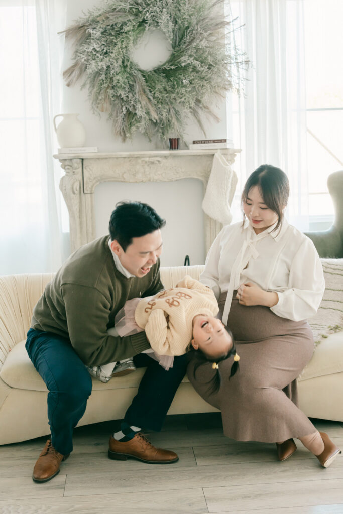 korean family holding toddler girl upside down laughing while mom hold her pregnant belly