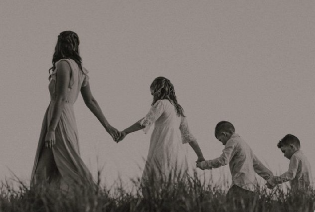 mom leading the ling holding hands with each kid in succession of age in a field