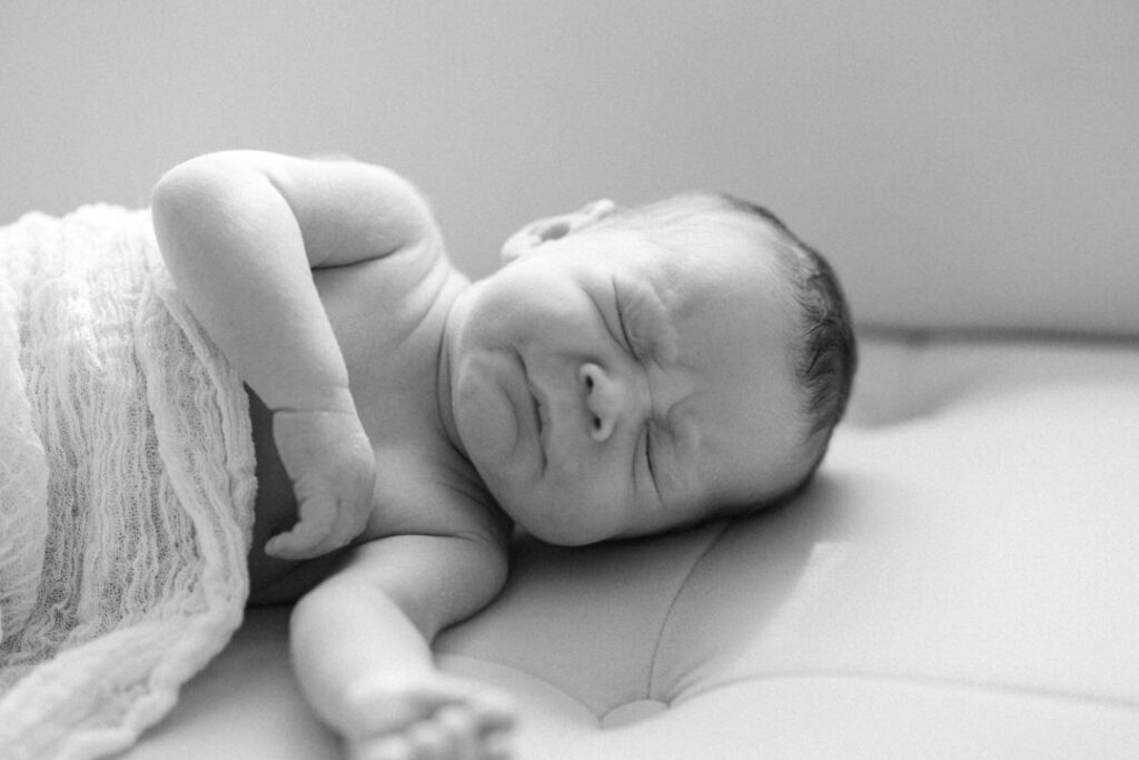 newborn baby wrapped in knit blanket sneezing