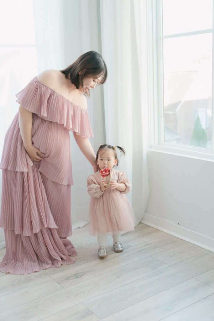 pregnant mom supporting belly while helping her small toddler girl