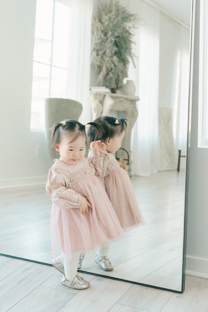 toddler playing at a large mirror in cute pink dress