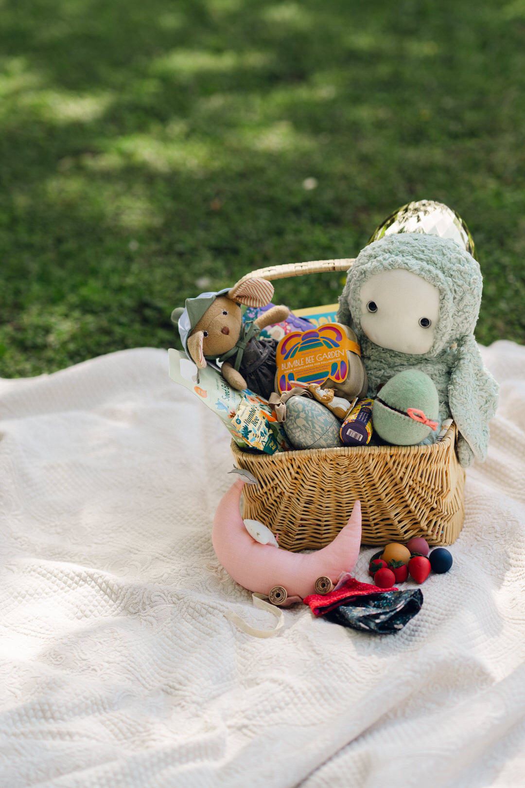 a filled easter basket in a vintage thrifted basket on a cream heirloom picnic blanket in the grass